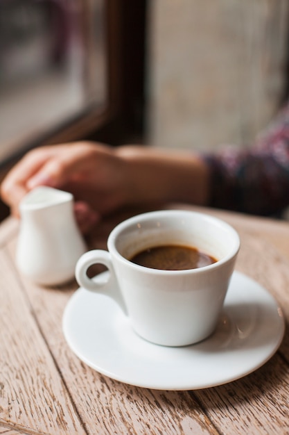Tazza di caffè con il lanciatore di latte della tenuta della mano della donna di defocus nel caf�