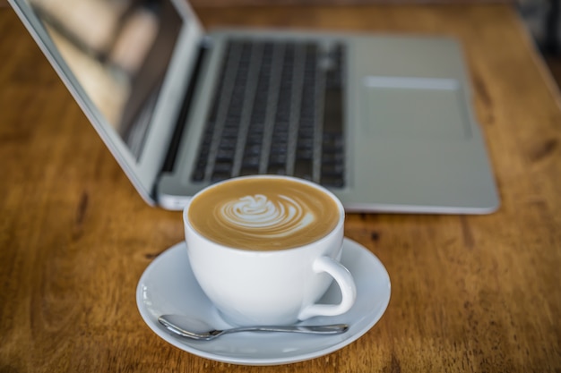 Tazza di caffè con un computer portatile dietro