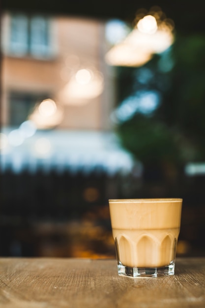 Tazza di caffè di vetro sullo scrittorio di legno con il contesto di caf� di defocus