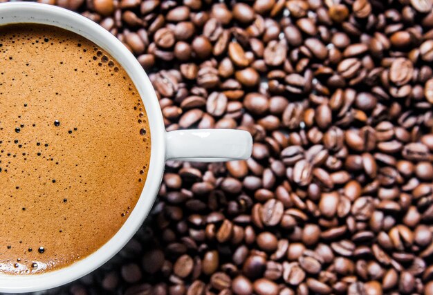 Tazza di caffè e chicchi di caffè sul tavolo, vista dall&#39;alto, caffè d&#39;amore, chicchi di caffè marrone isolato su sfondo bianco, tazza di caffè caldo con chicchi di caffè