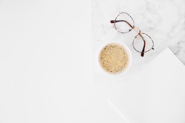 Tazza di caffè ed occhiali con carta bianca su fondo bianco