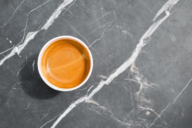 Tazza di caffè espresso caldo in una tazza di carta da asporto su un tavolo di pietra in uno sfondo monotono di caffè con pausa caffè spazio copia