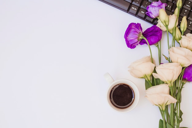 Tazza di caffè; fiori di eustoma bianchi e viola con tastiera su sfondo bianco