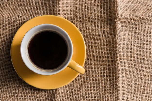 Tazza di caffè gialla con piastra su tela di sacco