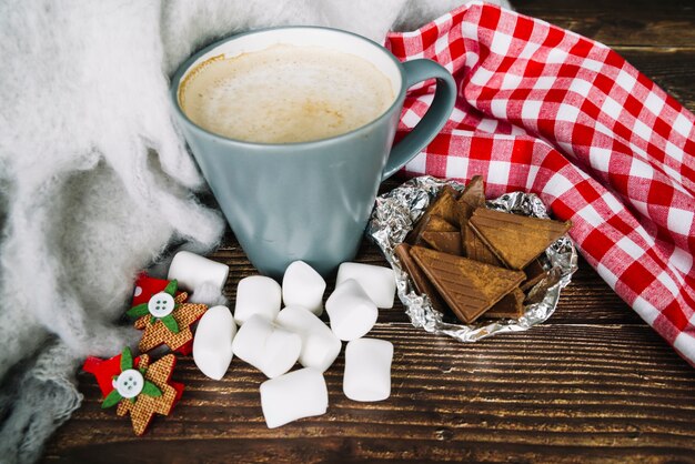 Tazza di caffè; pezzi di cioccolato e marshmallow sullo scrittorio di legno in natale