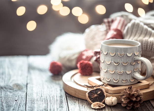 Tazza di caffè sopra bokeh di luci di Natale in casa sul tavolo di legno con maglione su una parete e decorazioni. Decorazione natalizia, magico Natale