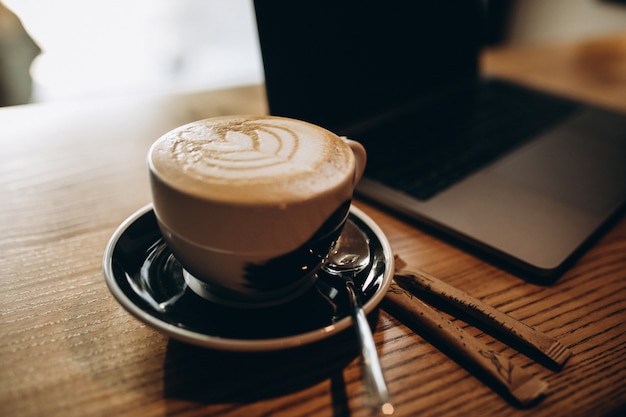 Tazza di caffè sul tavolo vicino al computer portatile