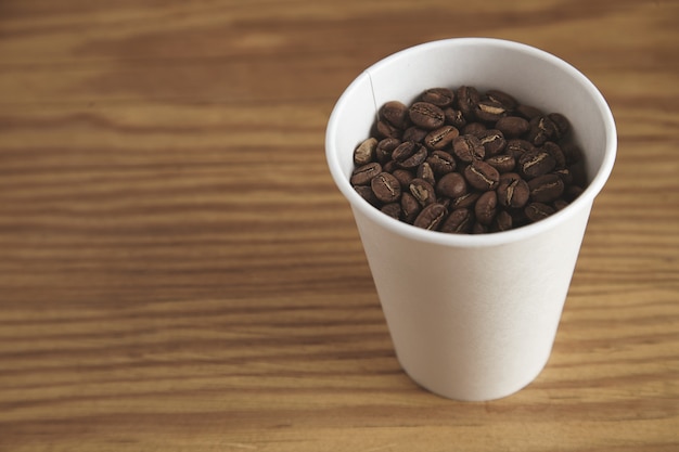 Tazza di carta bianca vuota con buoni chicchi di caffè tostati su un tavolo di legno spesso nel negozio di caffè