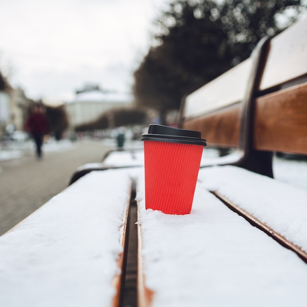 Tazza di carta rossa si trova sulla panchina nevicata in vicolo