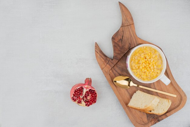 Tazza di mais dolce con fetta di pane su tavola di legno.