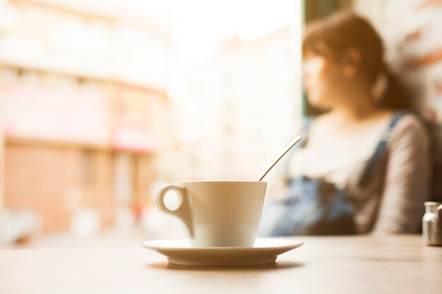 Tazza di tazza di caffè davanti alla donna di defocus che osserva via