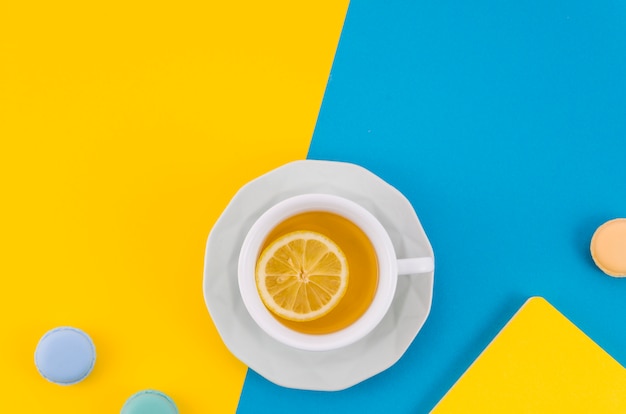 Tazza di tè al limone con amaretti su doppio fondale giallo e blu