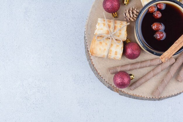 Tazza di tè con cinorrodi, biscotti e palline su tavola di legno.