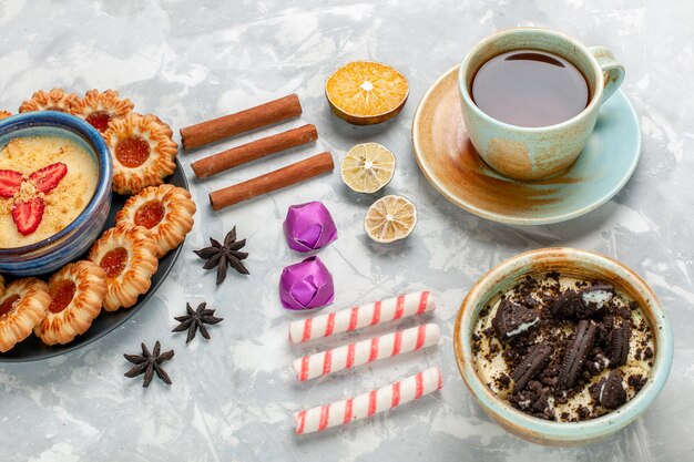 Tazza di tè con vista a metà superiore con dessert di biscotti al cioccolato e biscotti con marmellata su torta di cioccolato bianco chiaro biscotto da scrivania cuocere la torta di zucchero dolce