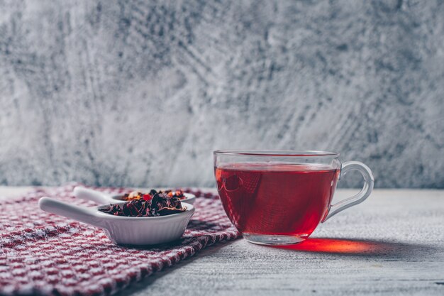 tazza di tè con vista laterale di erbe di tè su uno sfondo grigio con texture