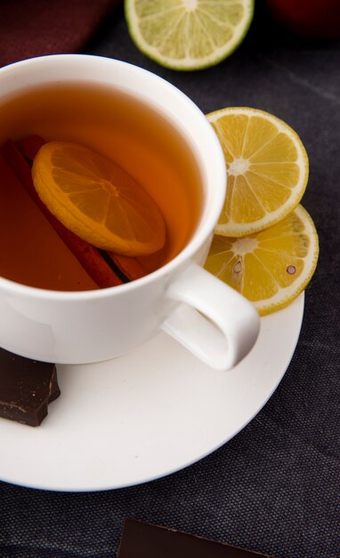Tazza di tè di vista laterale con cioccolato fondente alla cannella e lime sulla superficie nera