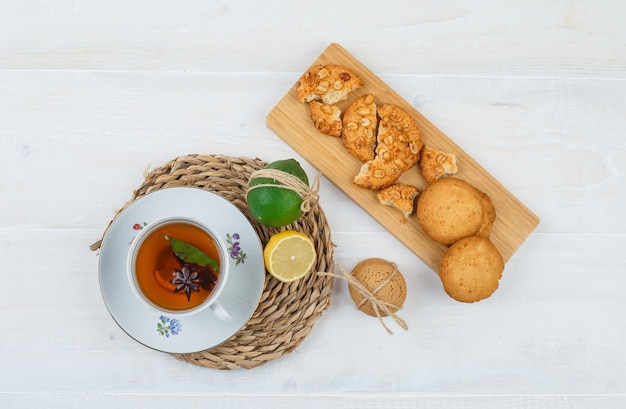 Tazza di tè e agrumi con i biscotti su un tagliere su una tovaglietta rotonda sulla superficie bianca