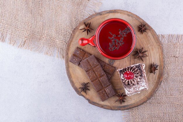 Tazza di tè, fetta di torta e barretta di cioccolato su un pezzo di legno. Foto di alta qualità