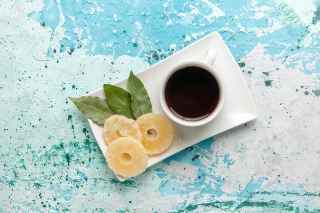 Tazza di tè vista dall'alto con anelli di ananas essiccati su superficie azzurra