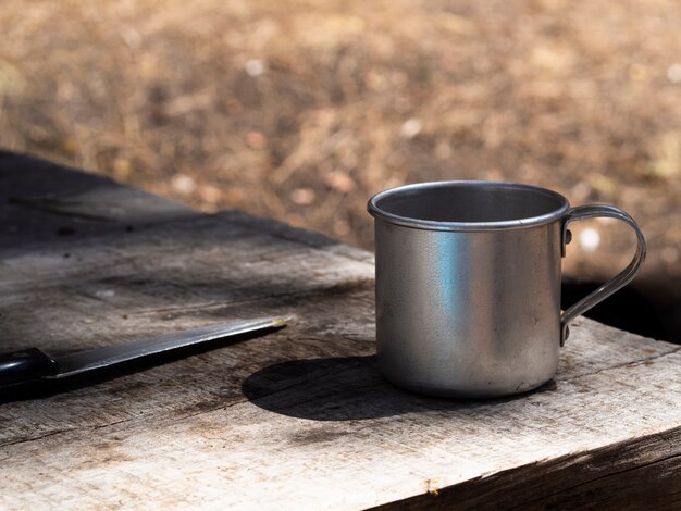 Tazza e coltello d'annata del metallo sulla tavola di legno misera