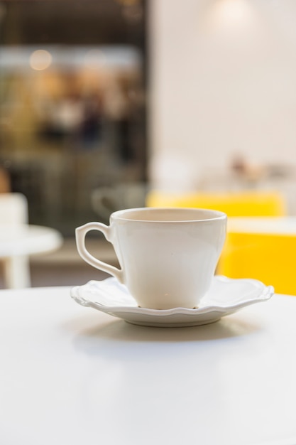 Tazza e piattino di ceramica sulla tavola bianca contro il fondo della sfuocatura