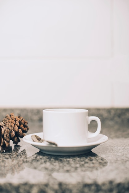 Tazza e piattino in ceramica bianca su tavolo in marmo riflettente