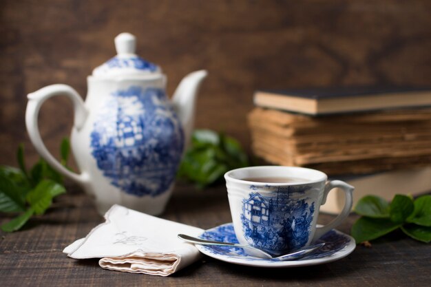 Tazza e teiera di tè antiche della porcellana con i libri e tovagliolo piegato sulla tavola di legno