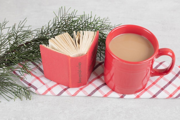 Tazza rossa e libro sulla tovaglia con ramo di pino