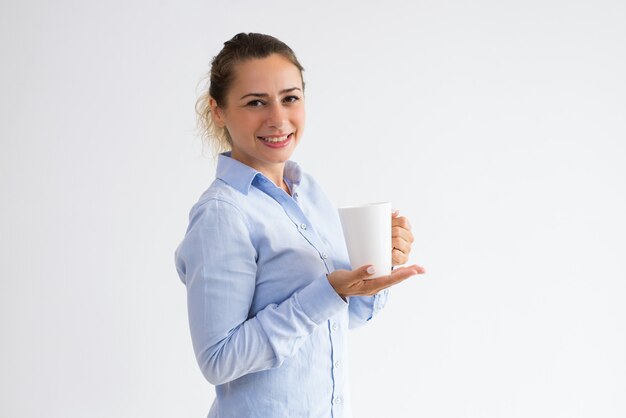 Tazza sorridente della tenuta della donna graziosa ed esaminare macchina fotografica