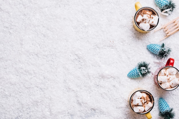 Tazze con marshmallow e bevande vicino giocattoli di Natale tra la neve