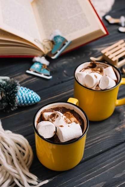 Tazze con marshmallow vicino a giocattoli di Natale e libro