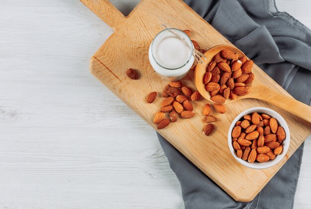 Tazze piatte di latte con nocciole, mandorle e noci diverse su fondo di legno bianco. orizzontale