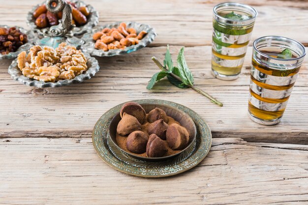 Tazze vicino a ramoscello vegetale, dolci al cioccolato, frutta secca e noci a bordo