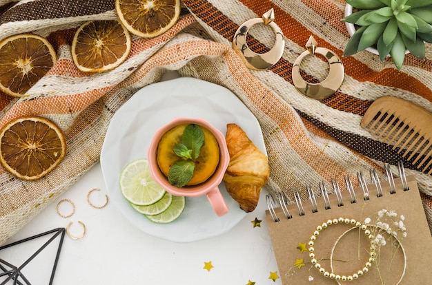 Tè al limone alle erbe con croissant e accessori femminili sulla tovaglia su sfondo bianco