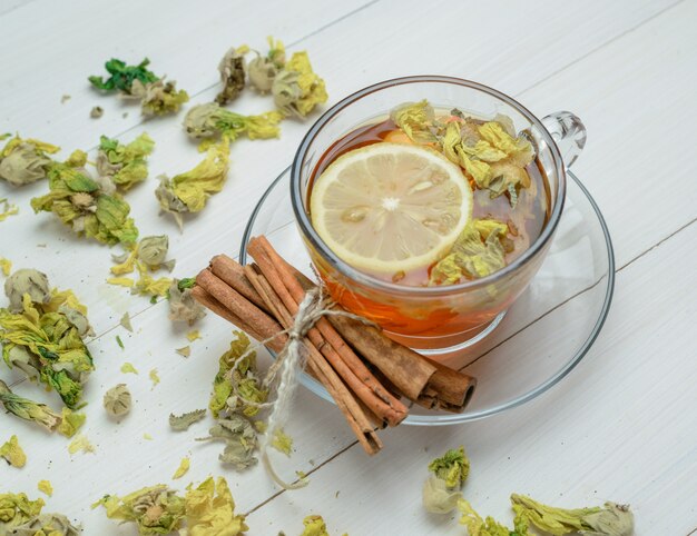 Tè al limone con erbe secche, bastoncini di cannella in una tazza su superficie di legno, vista di alto angolo.