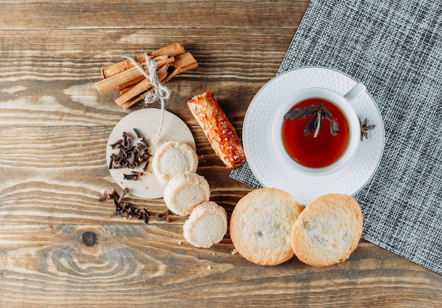 Tè alla menta con bastoncini di cannella, biscotti, chiodi di garofano in una tazza su superficie di legno