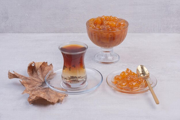 Tè aromatico caldo con foglie e marmellata sul tavolo bianco.