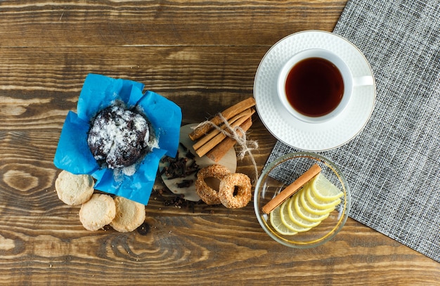 Tè con biscotti, chiodi di garofano, fette di limone, bastoncini di cannella in una tazza su superficie di legno