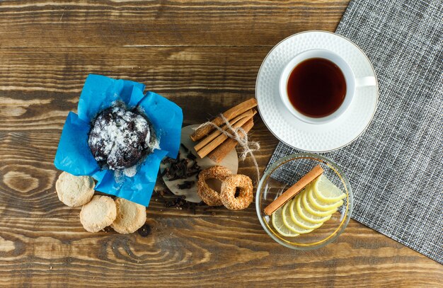 Tè con biscotti, chiodi di garofano, fette di limone, bastoncini di cannella in una tazza su superficie di legno