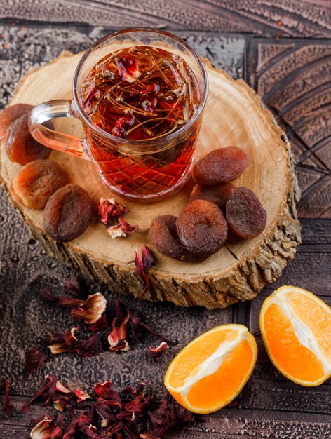 Tè con frutta secca, erbe, arancia, legno in una tazza sulla superficie delle piastrelle di pietra