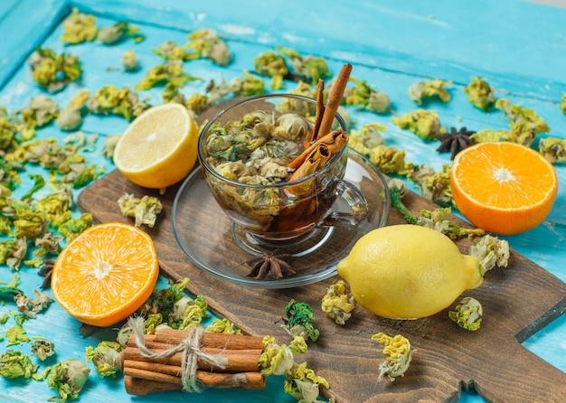 Tè con spezie, arancia, limone, erbe secche in una tazza su blu e tagliere, ad alto angolo di visione.