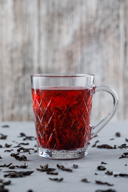 Tè con tè nero secco in una tazza di vetro su gesso e superficie sgangherata