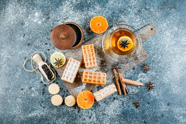 Tè in tazza con cialda, biscotto, spezie, patatine fritte, vista dall'alto arancione su sgangherata e tagliere