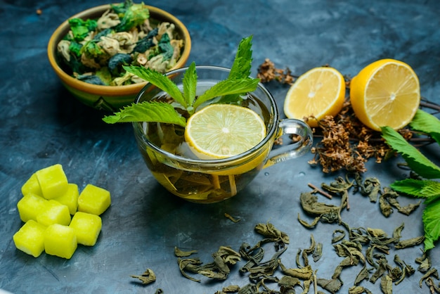 Tè in una tazza con menta, erbe essiccate, limone, zollette di zucchero ad alto angolo di vista su una superficie blu