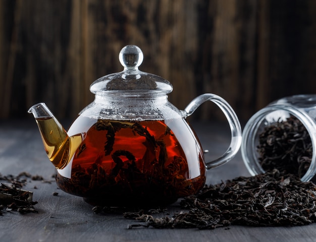 Tè nero con tè asciutto in una teiera su superficie di legno, vista laterale