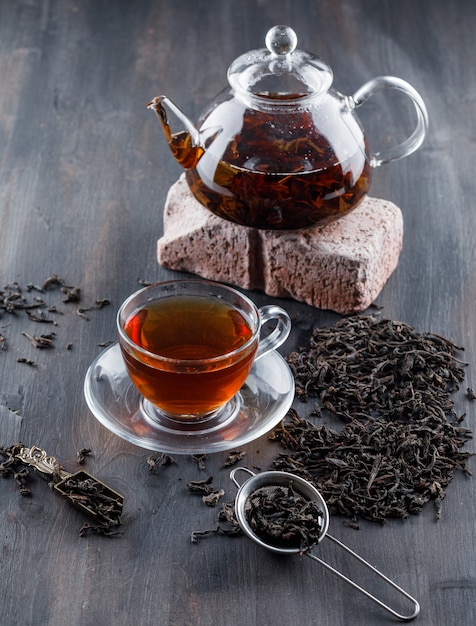 Tè nero in teiera e tazza con tè asciutto, vista dell'angolo alto del mattone su una superficie di legno