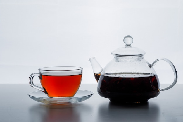 Tè preparato nella vista laterale della tazza e della teiera su una superficie bianca di pendenza