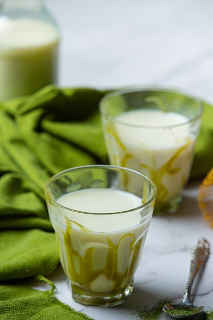 Tè verde caldo in un bicchiere con crema condita con tè verde, decorato con tè verde in polvere.