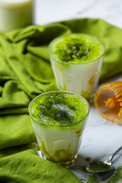 Tè verde caldo in un bicchiere con crema condita con tè verde, decorato con tè verde in polvere.