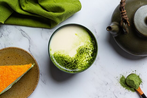 Tè verde caldo in un bicchiere con crema condita con tè verde, decorato con tè verde in polvere.